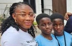 Alli Condemns Ex-Minister Adelabu’s Sister’s Abduction, Urges Swift Rescue Three people posing for a photo outside a building: an adult woman with glasses and two young boys in blue shirts, all smiling at the camera.