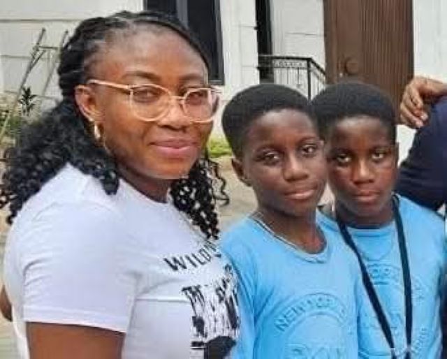 Bayo sister Three people posing for a photo outside a building: an adult woman with glasses and two young boys in blue shirts, all smiling at the camera.