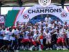 Gov. Mbah Splashes ₦150m Cash, Plot Of Land On Rangers Players, Officials For 2025/26 NPFL Title Win Nigerian football team celebrating 2025/2026 NPFL championship, posing with the trophy under a large 'Champions' arch.