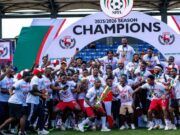 Gov. Mbah Splashes ₦150m Cash, Plot Of Land On Rangers Players, Officials For 2025/26 NPFL Title Win Nigerian football team celebrating 2025/2026 NPFL championship, posing with the trophy under a large 'Champions' arch.