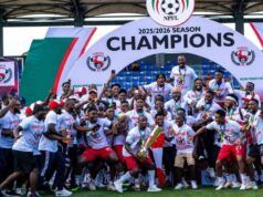 Gov. Mbah Splashes ₦150m Cash, Plot Of Land On Rangers Players, Officials For 2025/26 NPFL Title Win Nigerian football team celebrating 2025/2026 NPFL championship, posing with the trophy under a large 'Champions' arch.