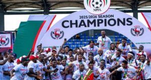 Gov. Mbah Splashes ₦150m Cash, Plot Of Land On Rangers Players, Officials For 2025/26 NPFL Title Win Nigerian football team celebrating 2025/2026 NPFL championship, posing with the trophy under a large 'Champions' arch.