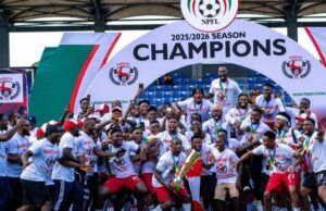 Gov. Mbah Splashes ₦150m Cash, Plot Of Land On Rangers Players, Officials For 2025/26 NPFL Title Win Nigerian football team celebrating 2025/2026 NPFL championship, posing with the trophy under a large 'Champions' arch.