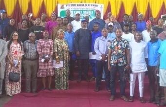 Oyo Assembly Assures Cleaner, Healthier Environment As Public Hearing On Single-Use Plastics Prohibition Bill Holds Group of men and women posing on a stage at a formal assembly event, with a banner in the background and yellow/red drapery behind them.