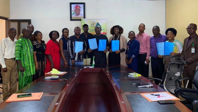 FCA Group of professionals around a conference table holding blue folders, suggesting a signing or agreement ceremony.