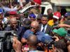 Oyo School Abduction: Obasa Reaffirms Push For State Police Amid NUT Protest Politician or speaker addressing a crowded media scrum with multiple cameras and microphones around him near a white vehicle.