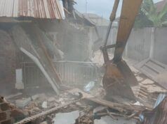 Makinde’s Govt Demolishes Building Used By Kidnappers Of Adelabu’s Sister, Nephews Excavator bucket amid collapsed brick walls and scattered debris at a demolition site with dust in the air.
