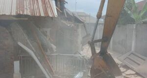 Makinde’s Govt Demolishes Building Used By Kidnappers Of Adelabu’s Sister, Nephews Excavator bucket amid collapsed brick walls and scattered debris at a demolition site with dust in the air.