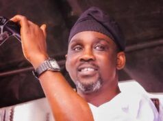 Pasuma Threatens Lawsuit Over Unauthorised Copyright Infringement Man on stage speaking into a microphone, wearing a black head wrap and white shirt, smiling at the audience.