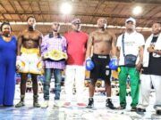 Glorious Promotions Stages ‘Fight Until The Killings Stop’ Boxing Show Group of boxers and coaches posing in a boxing ring; one fighter wears a championship belt across the waist.