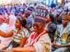Between Shettima’s Ekiti Visit And The Visit Ekiti Cap Crowd of people at a formal gathering, many wearing traditional hats and lanyards, seated in rows.
