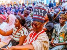 Between Shettima’s Ekiti Visit And The Visit Ekiti Cap Crowd of people at a formal gathering, many wearing traditional hats and lanyards, seated in rows.