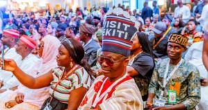 Between Shettima’s Ekiti Visit And The Visit Ekiti Cap Crowd of people at a formal gathering, many wearing traditional hats and lanyards, seated in rows.