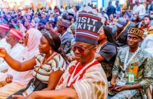 Between Shettima’s Ekiti Visit And The Visit Ekiti Cap Crowd of people at a formal gathering, many wearing traditional hats and lanyards, seated in rows.